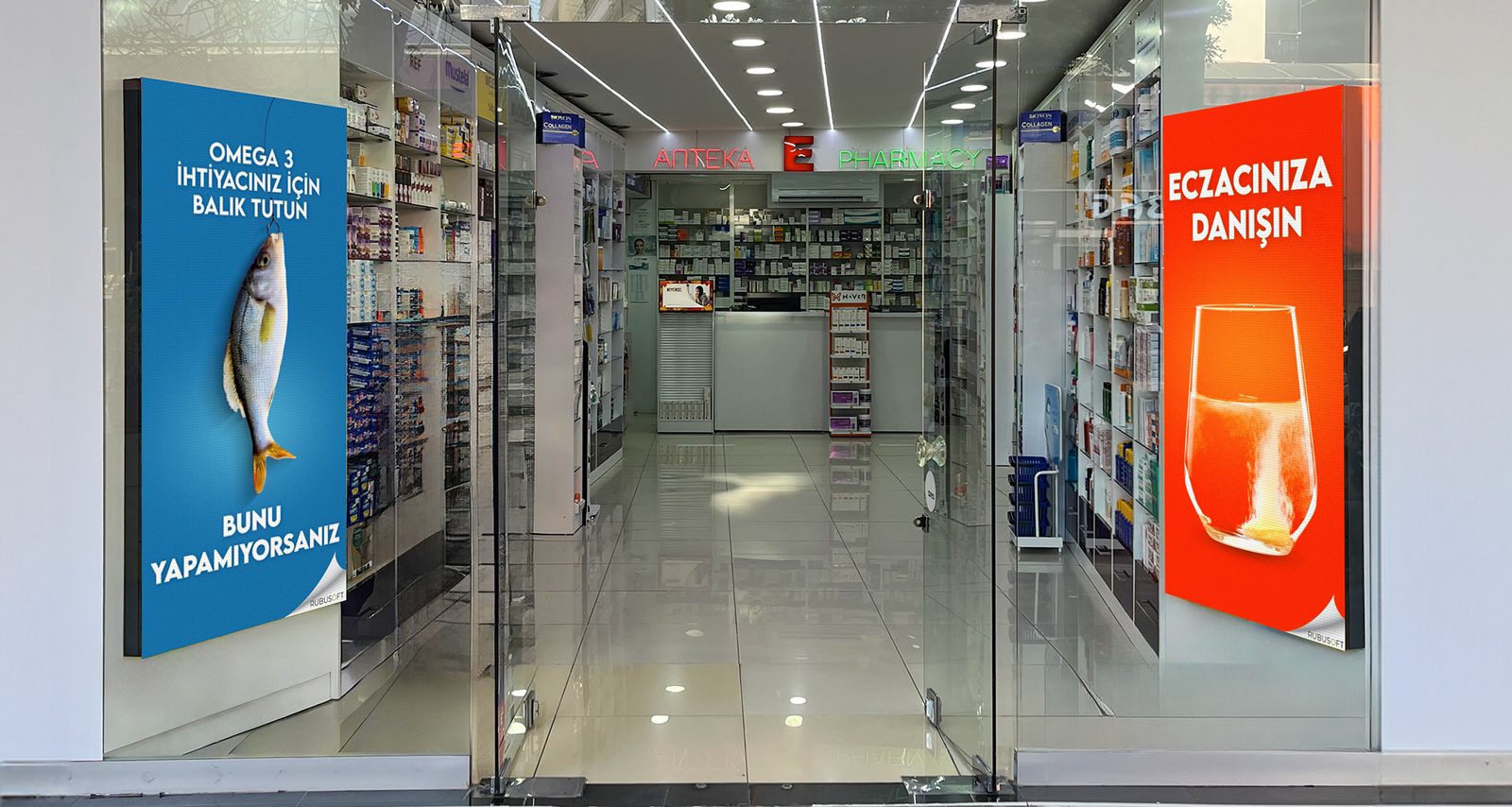 Bir eczanenin cam cephesinde, girişin iki yanında karşılıklı kurulu iki dikey tanıtım ekranı