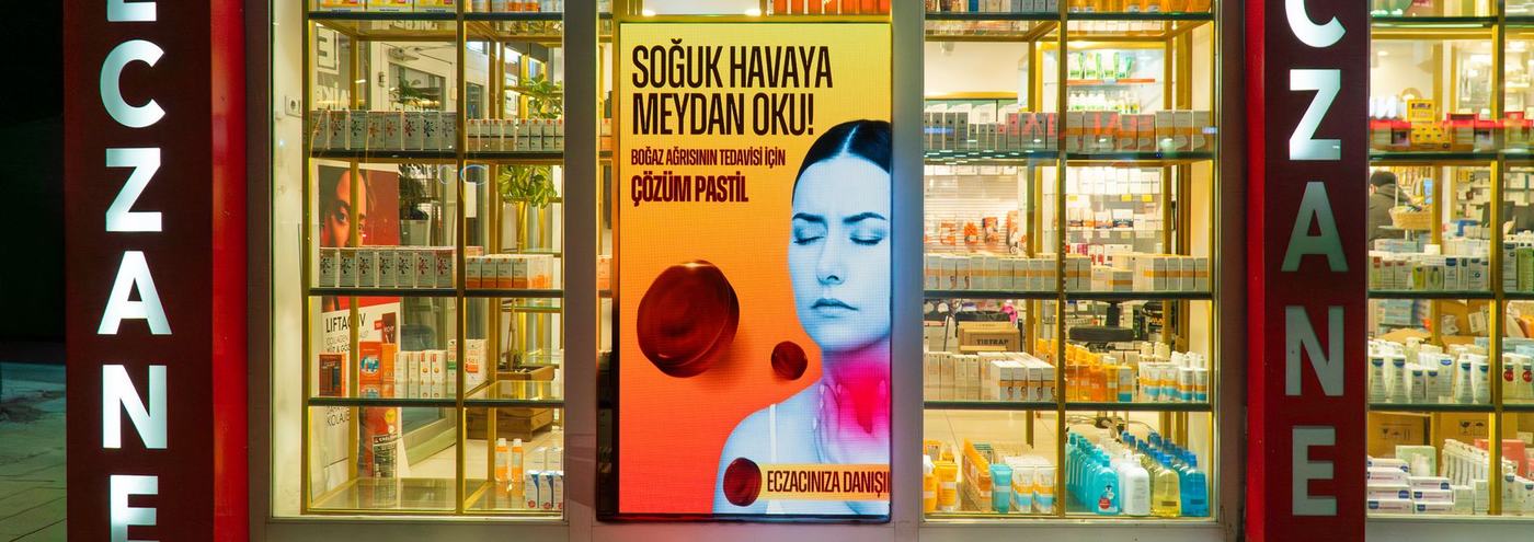 Vitrinde yayın yapan LED ekran, gece çekilmiş eczane cephesi