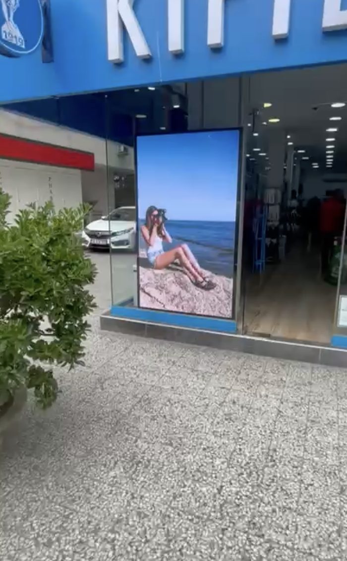 Bir mağaza vitrininde cam arkasına yerleştirilmiş, gün ışığında net okunan dikey LED ekran